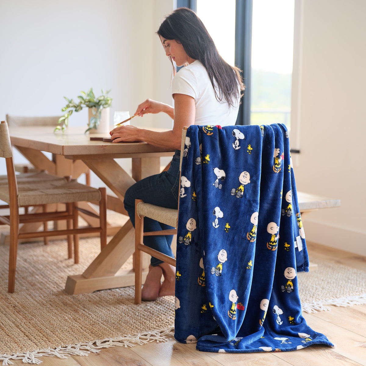 A woman sitting on a chair with a blue printed Peanuts throw blanket draped over the chair.