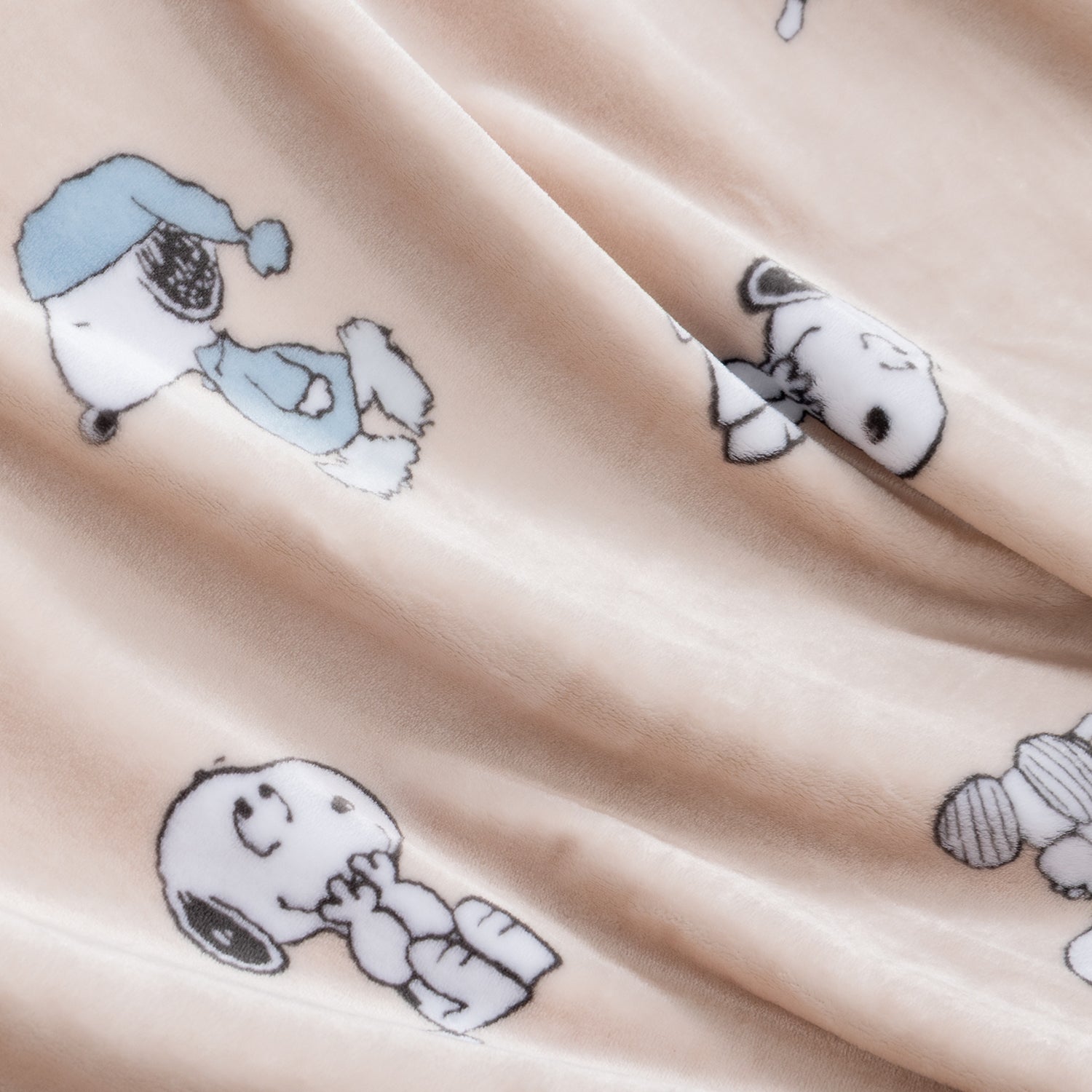 A close-up of a soft beige fabric with a repeating print of Snoopy lying down in black, white, and light blue.