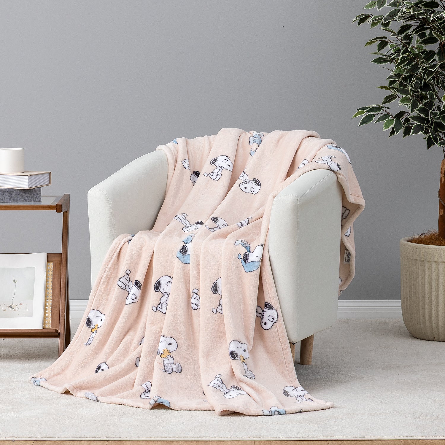 A light pink fleece throw blanket with a repeating cartoon dog print is draped over a white armchair in a styled living room setting.