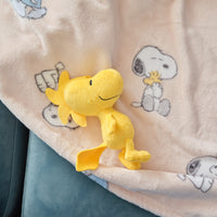 A woodstock plushie sitting on a blush Peanuts printed throw blanket.