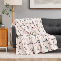 Beige blanket with cartoon dog pattern draped over a gray sofa in a living room.
