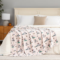 Bed with a pink blanket featuring cartoon characters, white pillows, and a wooden nightstand.