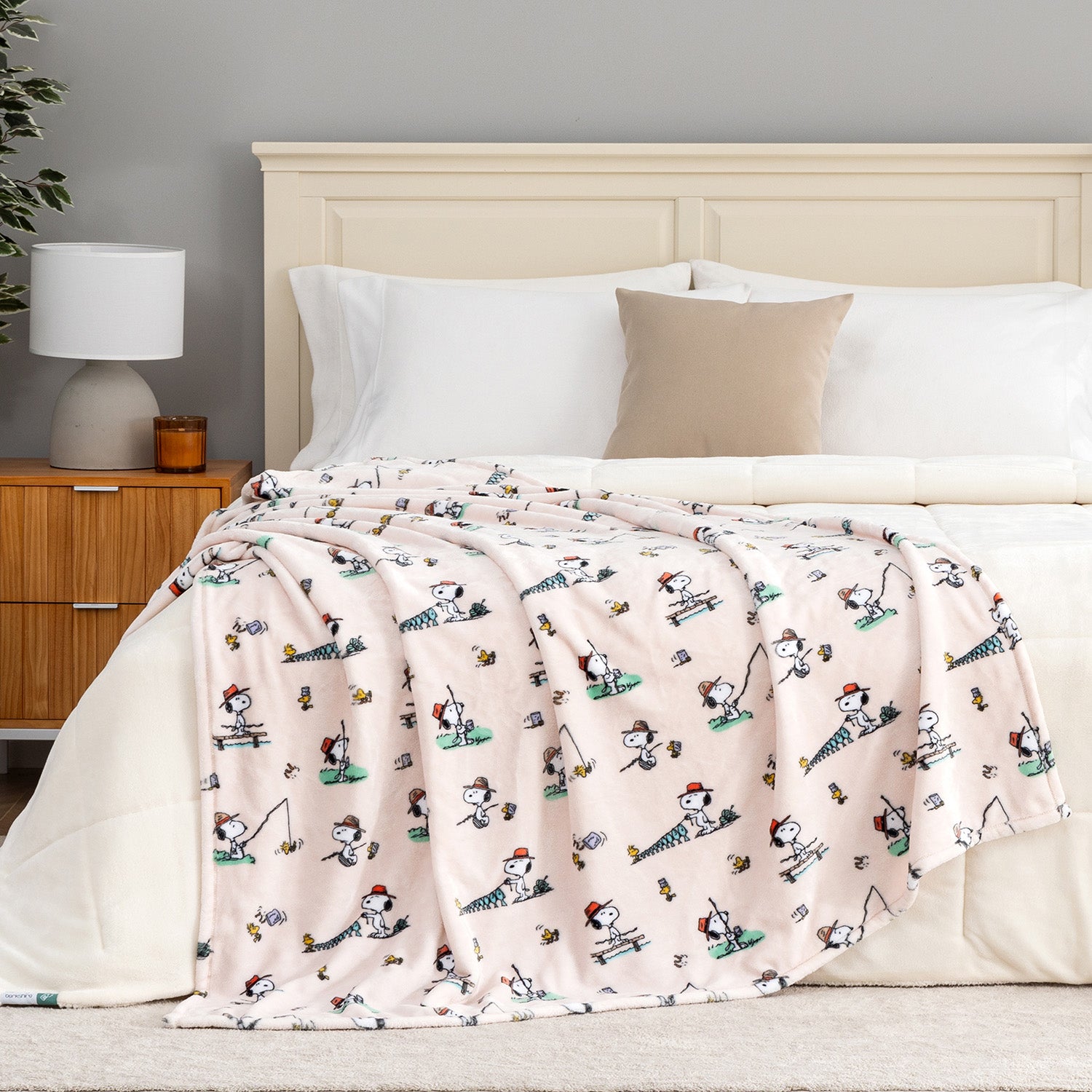 Bed with a pink blanket featuring cartoon characters, white pillows, and a wooden nightstand.
