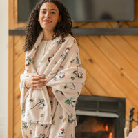 Woman wrapped in a patterned throw blanket standing in front of a fireplace.