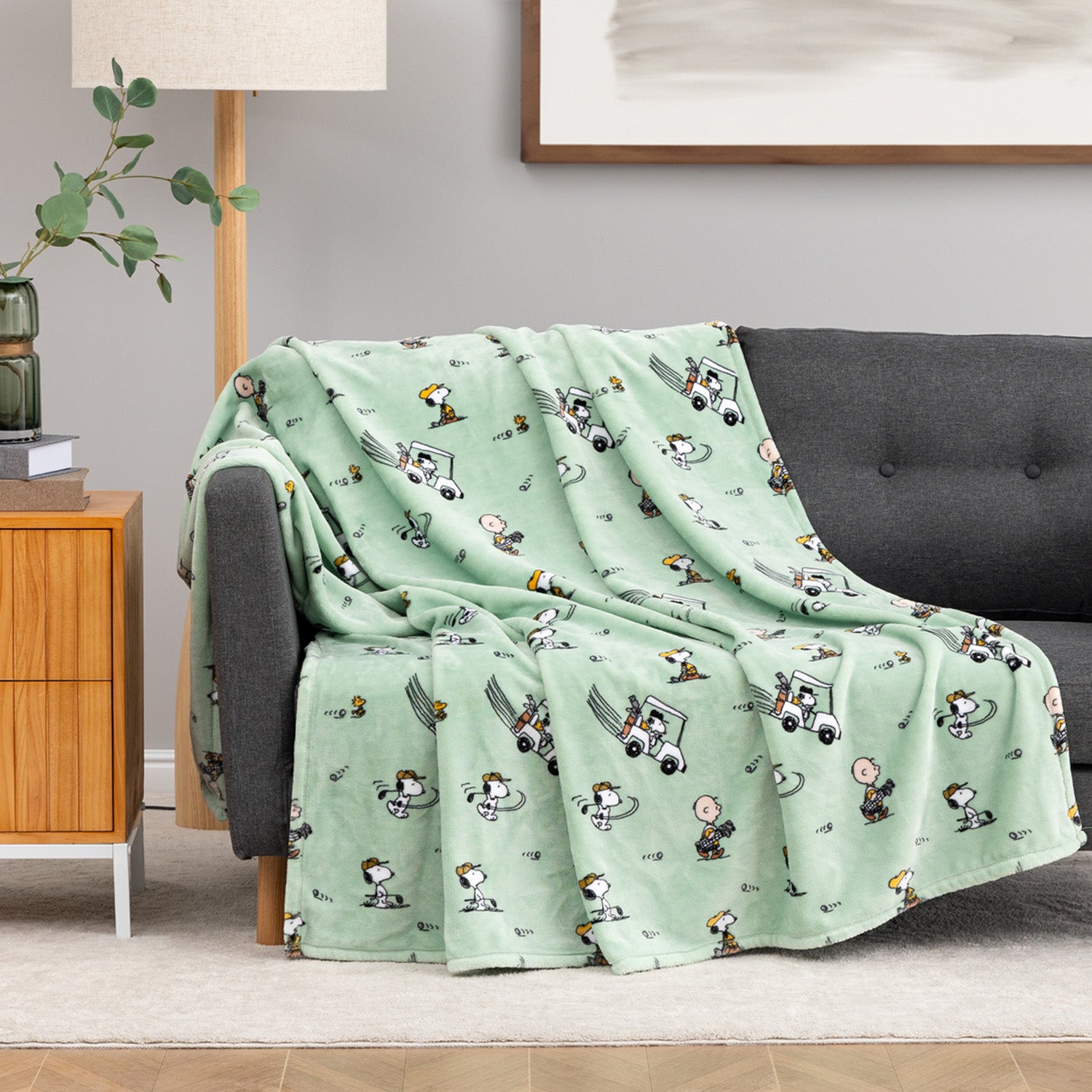 Green cartoon-themed blanket draped over a gray sofa in a living room.