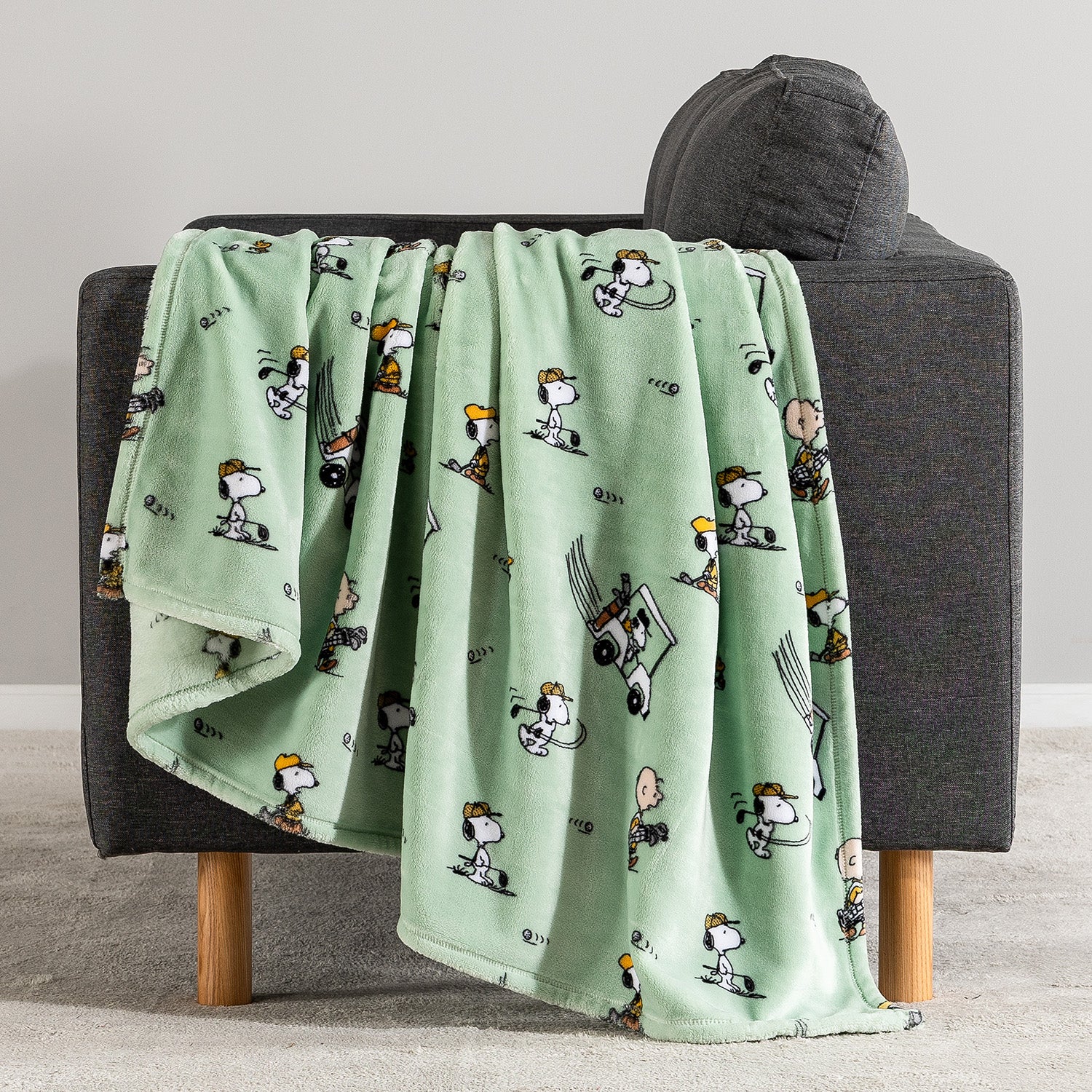 Green blanket with cartoon character pattern draped over a gray chair.