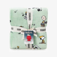Folded green blanket with Peanuts character patterns and a visible tag on a white background