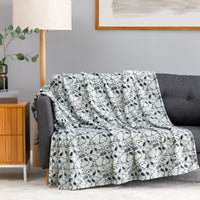 A light gray throw blanket with a black-and-white cartoon dog pattern is draped over a dark gray sofa in a living room setting.
