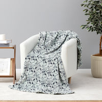 A light gray throw blanket with a black Snoopy and Woodstock cartoon pattern draped over a white armchair in a styled room setting.