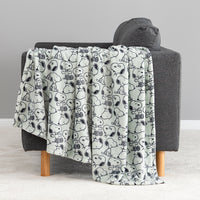 A light gray throw blanket with a black-and-white cartoon dog pattern is draped over a dark gray armchair with light wood legs in a minimalist room setting.