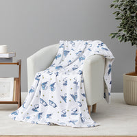 A white throw blanket with a blue cartoon dog pattern and small gold star accents, draped over a light gray armchair in a styled room setting.