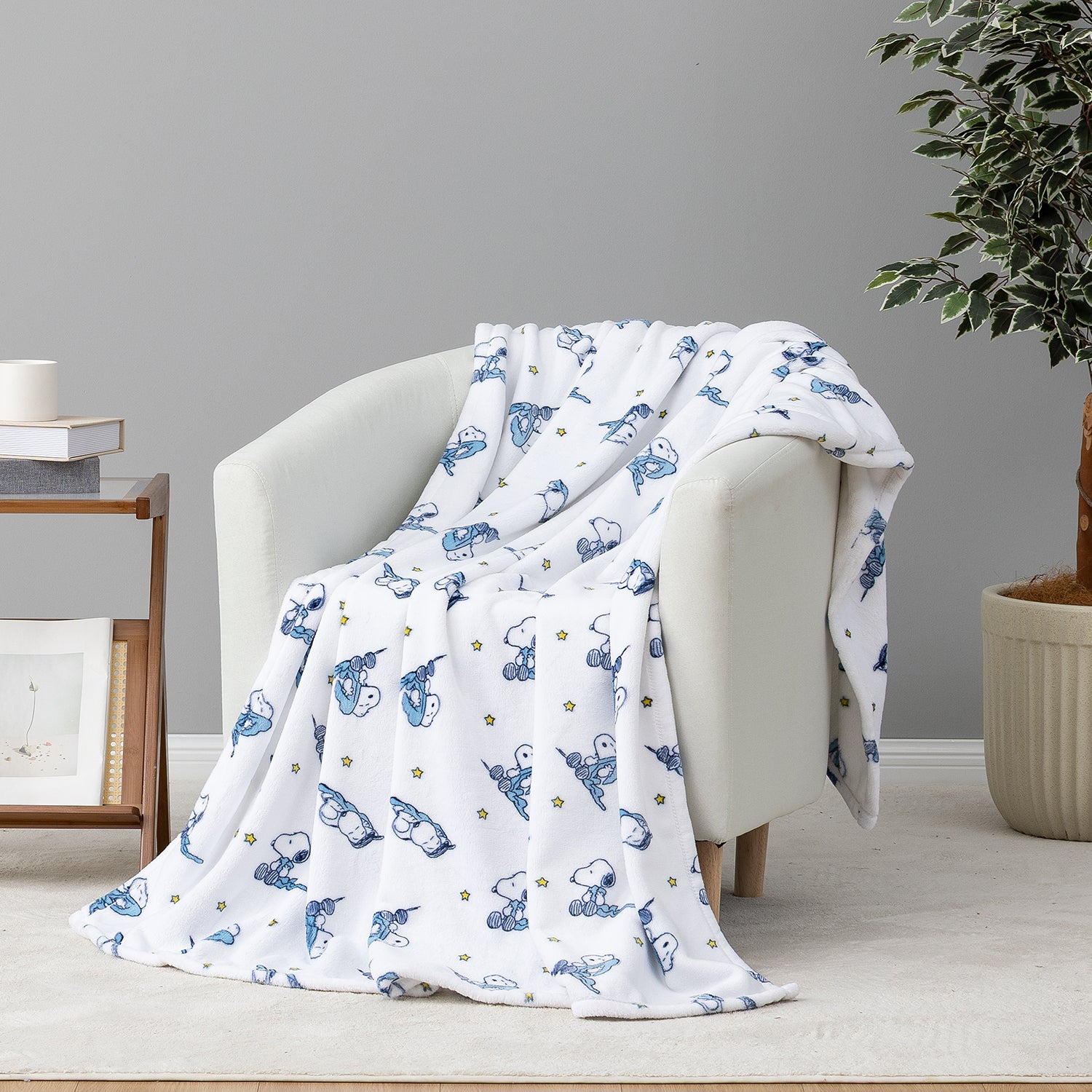 A white throw blanket with a blue cartoon dog pattern and small gold star accents, draped over a light gray armchair in a styled room setting.