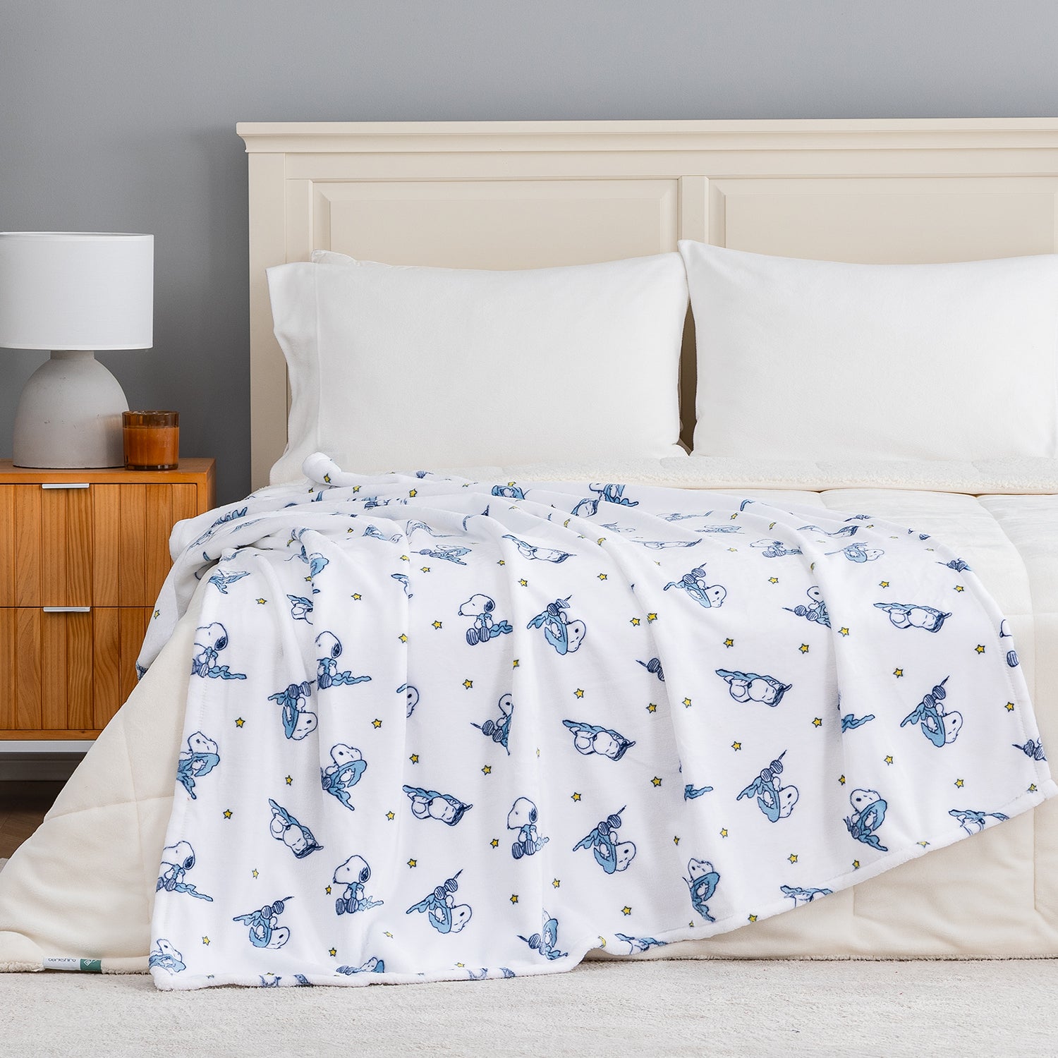 A white peanuts printed throw draped neatly over a beige bed.