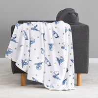 A white throw blanket with a blue cartoon dog and cat pattern and small yellow stars, draped over a dark gray armchair in a studio setting.