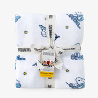 A folded white plush throw blanket with blue and yellow Peanuts cartoon prints, wrapped in a white ribbon printed with 'PEANUTS' and tied with a branded hangtag, on a light gray background.