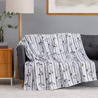 A throw blanket draped over a gray sofa in a living room setting, featuring a repeating cartoon character print on vertical gray and white stripes.