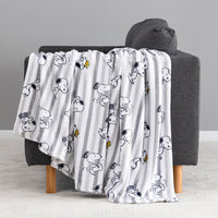 A white throw blanket with vertical gray stripes and a repeating cartoon dog print, draped over a dark gray armchair with wooden legs in a clean indoor setting.