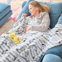 A woman laying on a blue sofa with a striped Peanuts throw blanket.