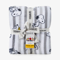 A folded Peanuts plush throw blanket with a white and gray striped pattern and cartoon character prints, tied with a white ribbon and tag.