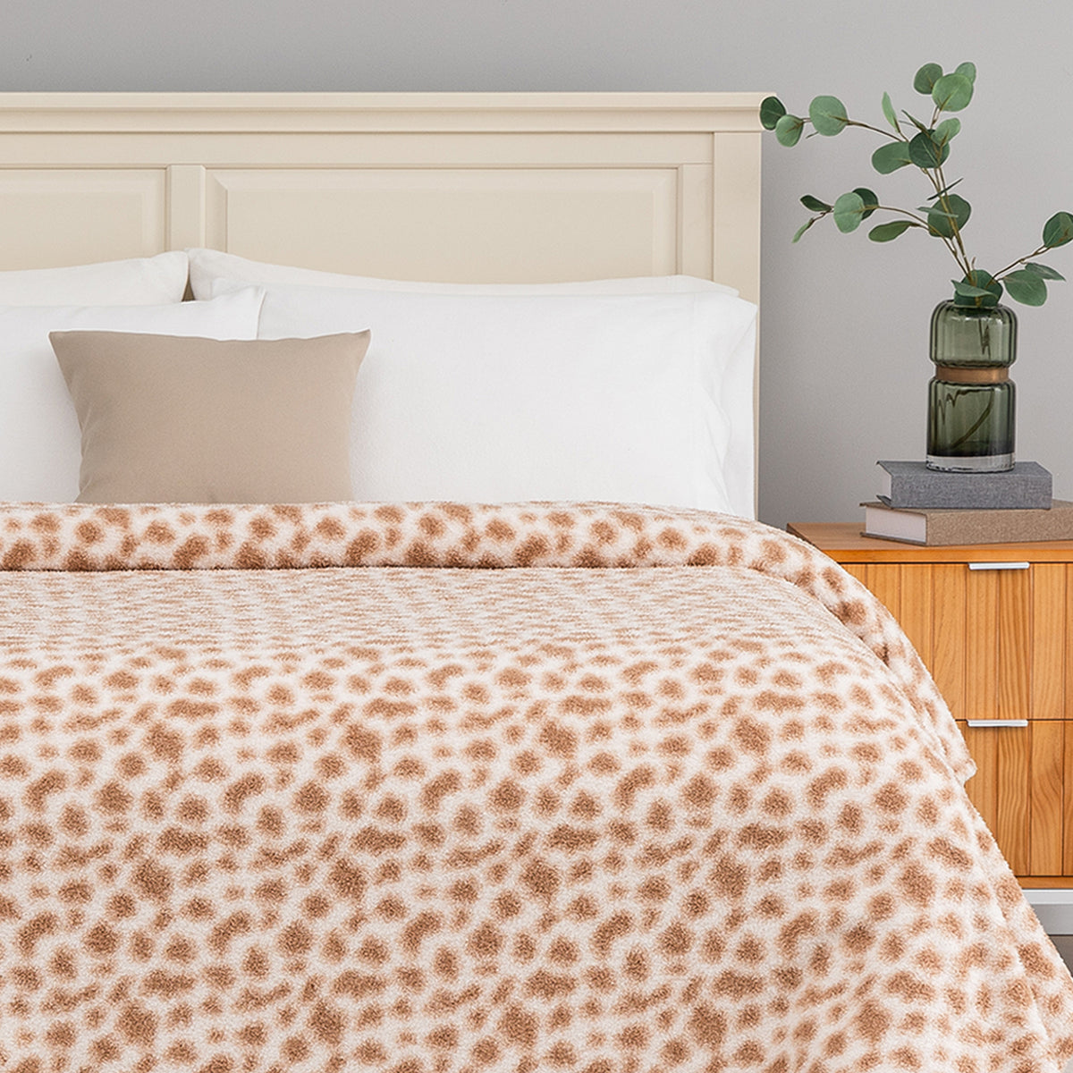 Bed with leopard print blanket, beige pillow, and wooden nightstand with plant.