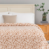 Bed with leopard print blanket, beige pillow, and wooden nightstand with plant.