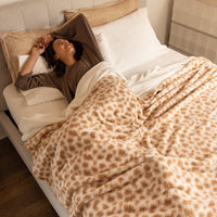 Woman lying in bed under a patterned blanket, smiling.