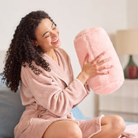 Woman in a pink robe holding a pink plush pillow  in a cozy living room.