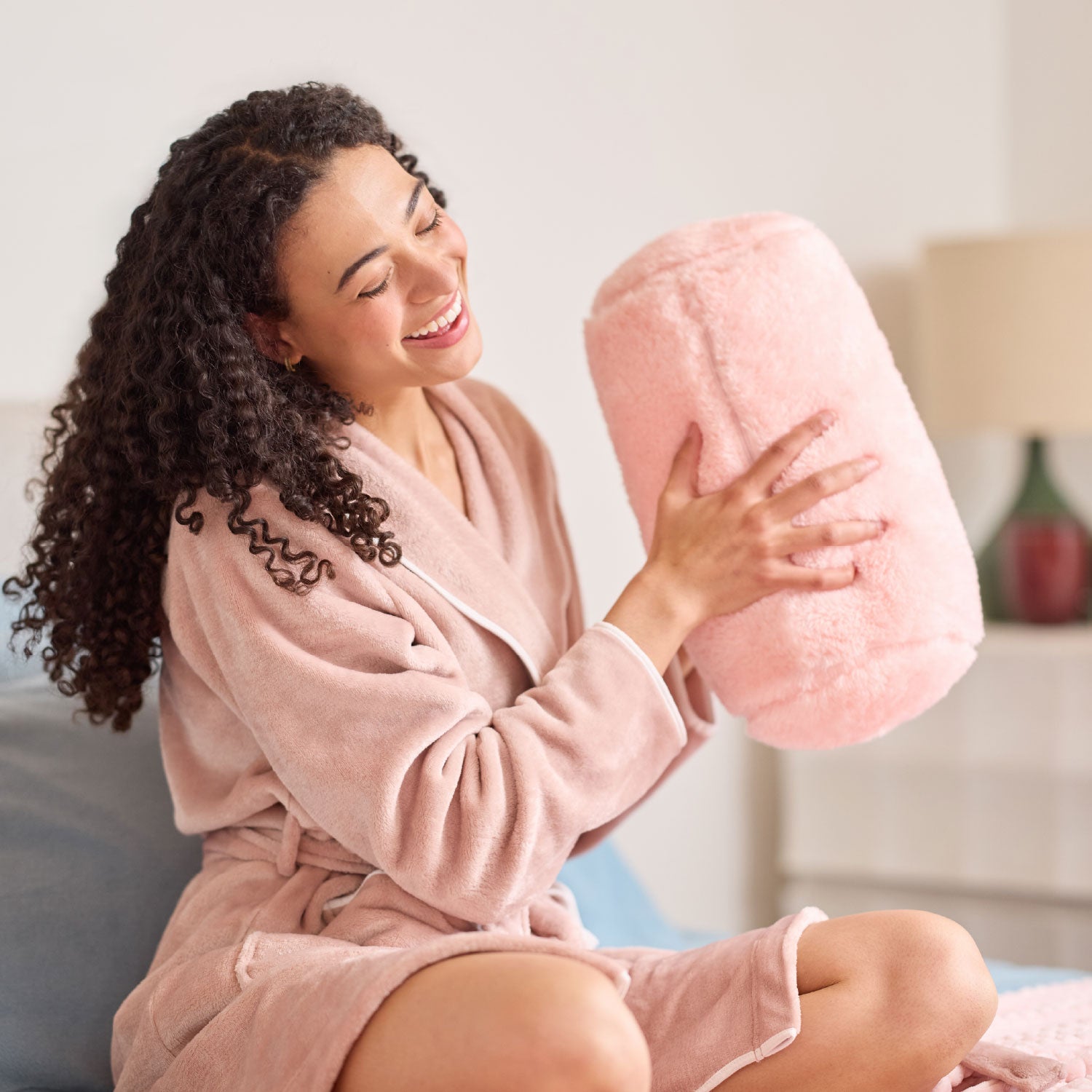Woman in a pink robe holding a pink plush pillow  in a cozy living room.