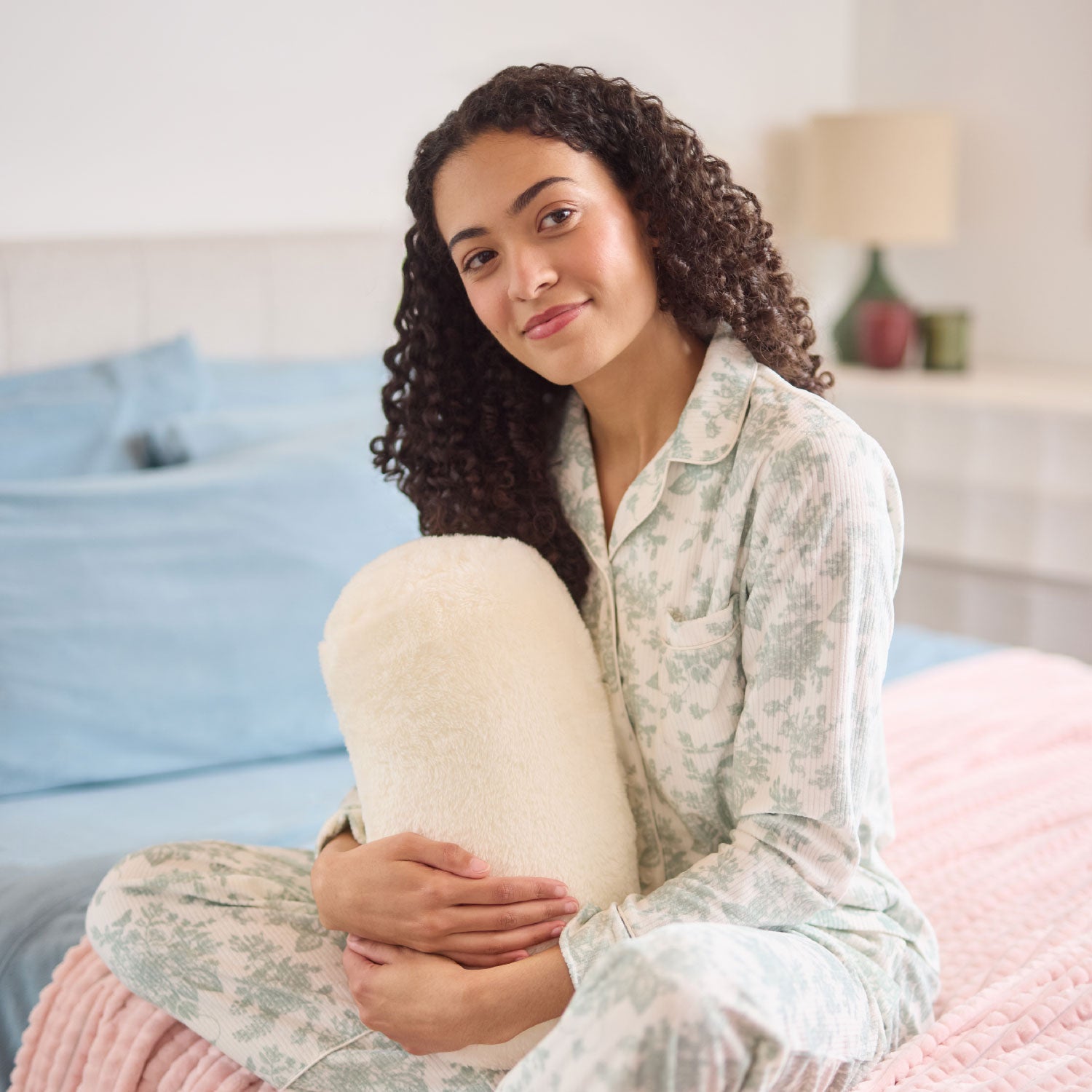 Woman in floral pajamas holding a white pillow in a bedroom setting.