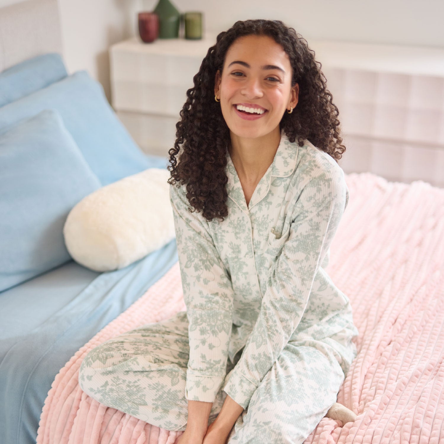 A model sitting and smiling on a cozy colorful bed.