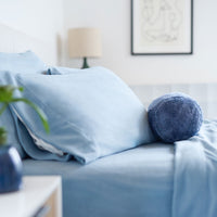 Light blue bedding on a bed with a decorative pillow in a bedroom setting.