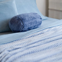 A blue waffle blanket decorated on a bed with a blue neckroll pillow.
