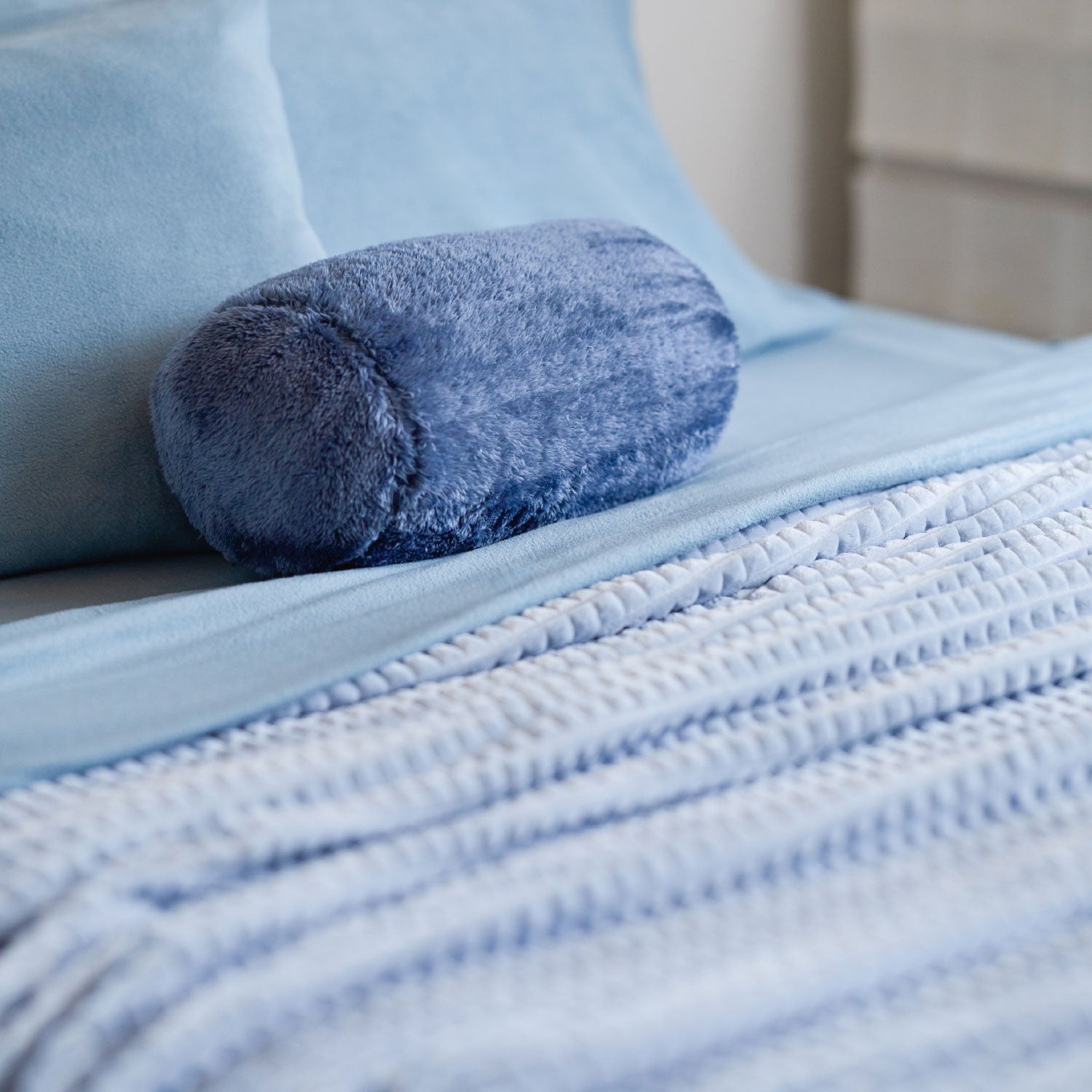 A blue waffle blanket decorated on a bed with a blue neckroll pillow.