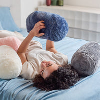 Person lying on a bed with large, round, plush pillows in various colors.