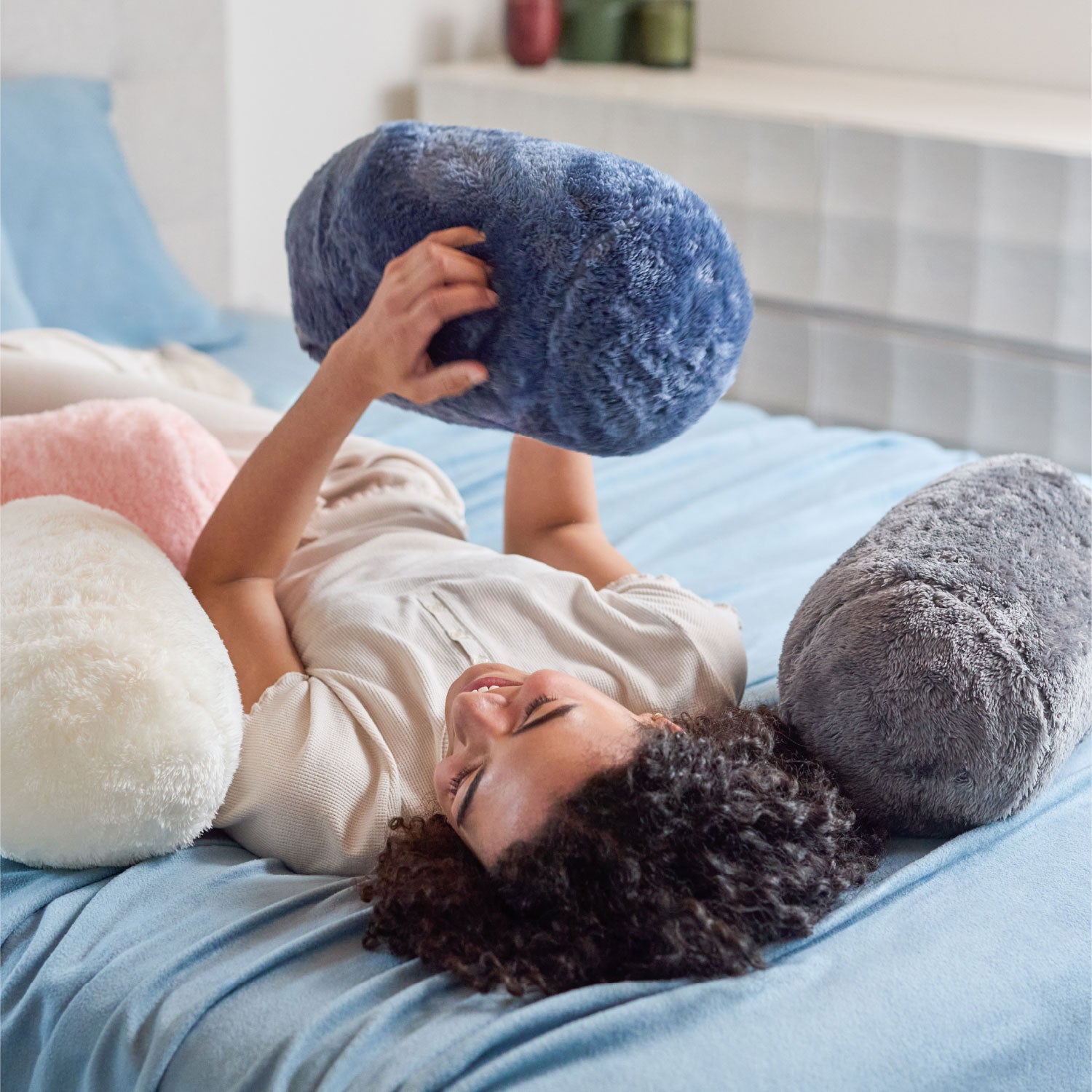 Person lying on a bed with large, round, plush pillows in various colors.