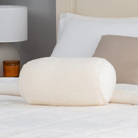 White fluffy pillow on a bed with a lamp and candle in the background