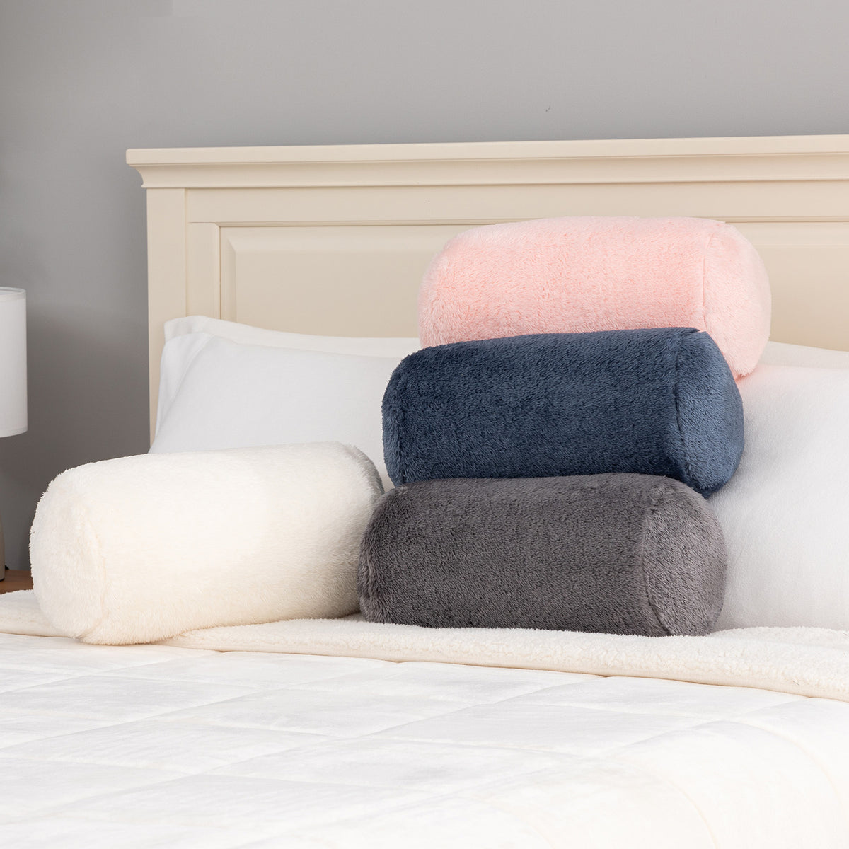 Stack of round and bolster pillows on a bed against a gray wall.
