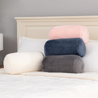 Stack of round and bolster pillows on a bed against a gray wall.