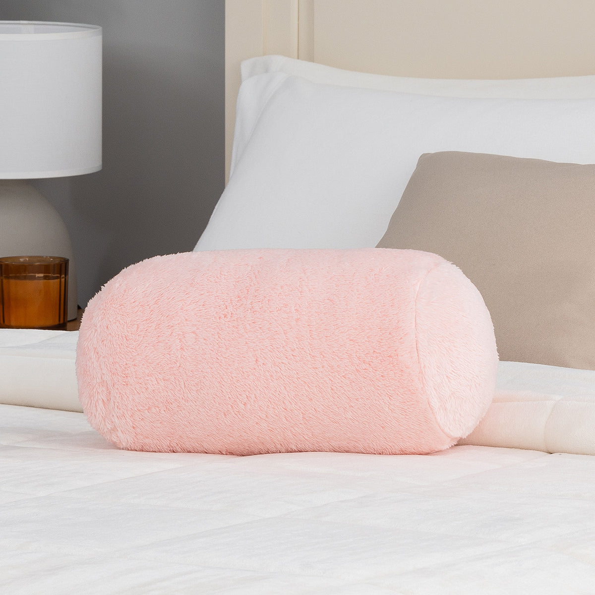 Pink cylindrical pillow on a bed with a lamp in the background