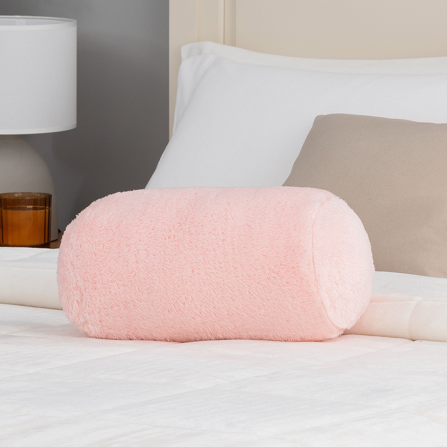 Pink cylindrical pillow on a bed with a lamp in the background