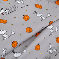 Light gray fabric with a repeating print of Snoopy and Woodstock in white, orange pumpkins, and small yellow stars, shown folded to display the pattern.