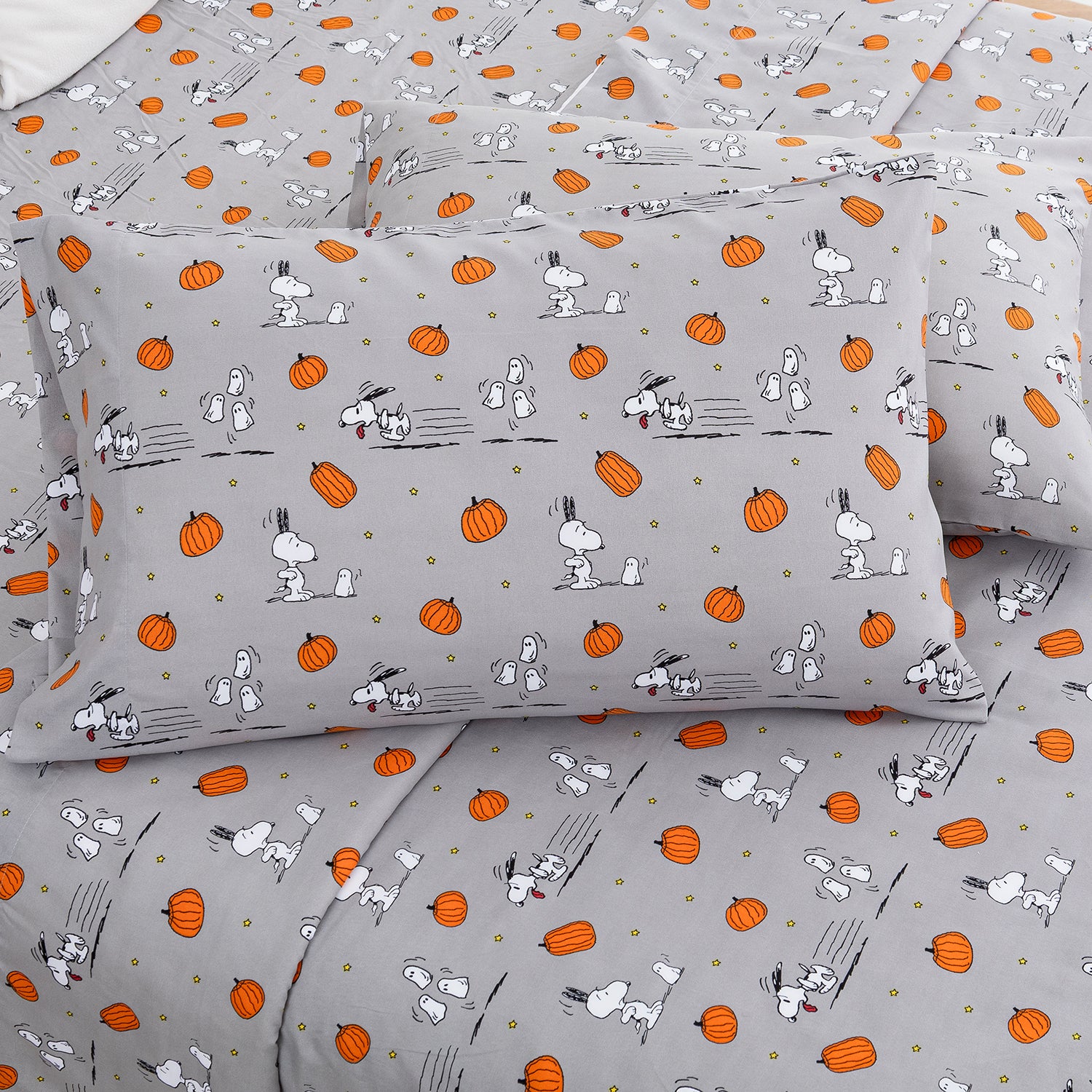 A gray bedding set with a repeating print of Snoopy and Woodstock alongside orange pumpkins and small gold dots, shown on a bed with two matching pillowcases.