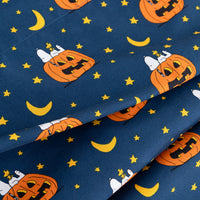 A close-up of patterned fabric featuring orange jack-o'-lanterns, yellow crescent moons, and yellow stars on a dark navy blue background. The fabric is draped to show its texture and print.