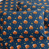 A close-up of a bedding set, likely pillowcases or a fitted sheet, featuring a Halloween pattern with orange jack-o'-lanterns, yellow crescent moons, and small yellow stars on a dark navy blue background.