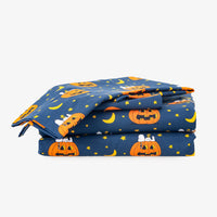 A folded navy blue fabric item, likely a blanket or comforter, featuring a Halloween print with orange jack-o'-lanterns, yellow crescent moons, and small white ghosts on a light gray background.