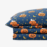 A stack of folded bedding, likely pillowcases or a fitted sheet set, featuring a dark navy blue Halloween pattern with orange jack-o'-lanterns, yellow crescent moons, and small yellow stars. The top pillowcase is shown flat, with the other layers folded underneath, set against a plain white studio background.