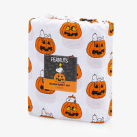 A packaged Halloween-themed Peanuts Queen Sheet Set on a clean white background. The sheets feature a white base with a repeating pattern of orange jack-o'-lantern pumpkins and Snoopy and Woodstock, with a black and orange Peanuts brand label wrapped around the front.