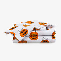 A folded white bedding set, likely a comforter or sheet set, featuring a repeating pattern of orange and black jack-o'-lantern pumpkins with Snoopy and Woody characters, shown on a plain light gray background.