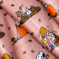 Pink fleece fabric with a printed cartoon pattern of Snoopy and Woodstock playing with falling autumn leaves, shown in a draped flat-lay arrangement.