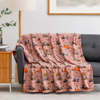A pink fleece throw blanket with a cartoon camping pattern is draped over a gray sofa in a living room setting.